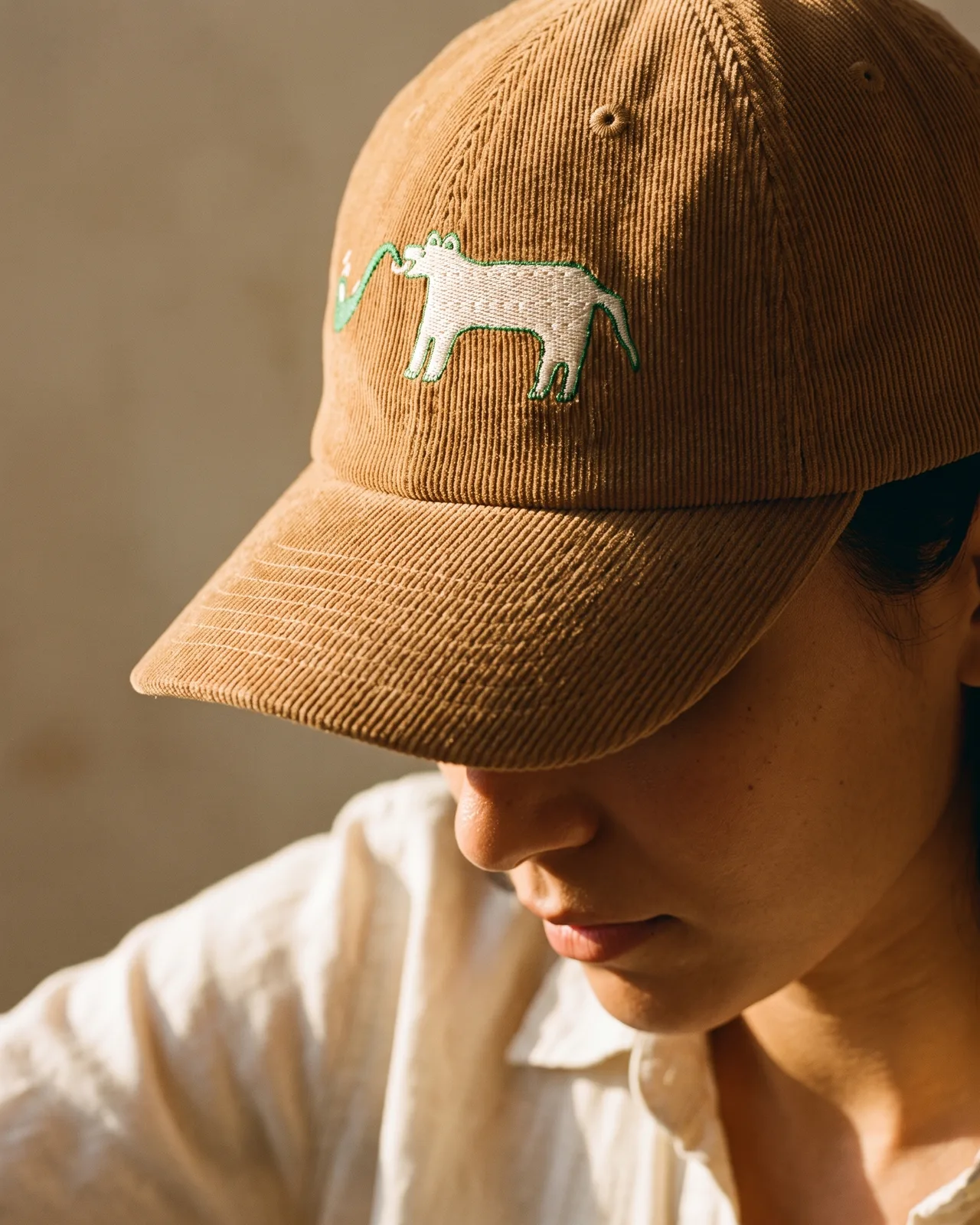 Woman in profile wearing the camel corduroy dad cap in warm window light